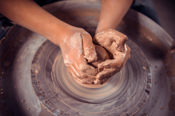 The potters hands are shaped a cup from a clay. The process of creating pottery on a potters wheel. The master ceramist works in his studio. Close-up, only hands. Crockery from clay own hands.