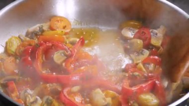 Kırmızı dolma biber parçaları ve sarı domates dilimleriyle tavada mantar pişirme şampiyonu. Yoğun bir duman içinde tahta kahverengi bir kaşıkla karıştırıyor.