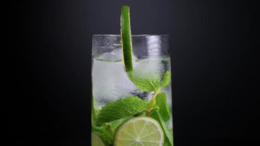 Limon dilimleri, nane yaprakları ve buz küpleriyle dönen bir mojito bardağının yakın çekimi.