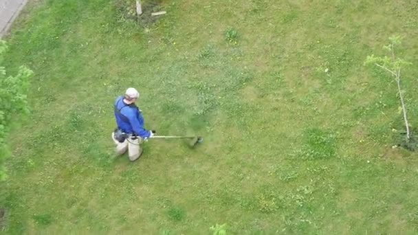 Вид сверху на человека в синей куртке, стригущего траву на газоне ручной газонокосилкой — стоковое видео