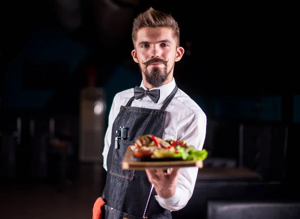 Νέος υπάλληλος εστιατορίου σερβίρει σαλάτα σε μαύρο φόντο. — Φωτογραφία Αρχείου