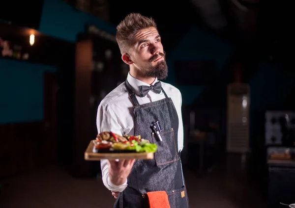 Karismatisk restaurang anställd betjänar hjälpsamt skålen på en svart bakgrund. — Stockfoto