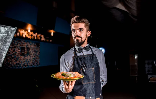 Επαγγελματίας φιλικό σερβιτόρος μεταφέρει ορεκτικό πιάτο σε μαύρο φόντο. — Φωτογραφία Αρχείου