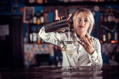 Karizmatik barmen kız meyhanedeki barın yanında dururken kokteyl yapma sürecini gösteriyor.