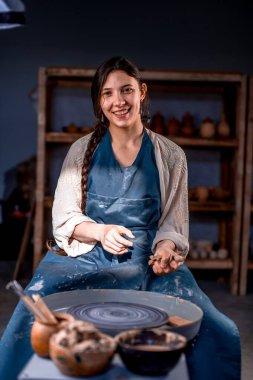 Toprak malzemesi yaparken poz veren yakışıklı bir zanaatkar. Sandalyede otururken önlük giyiyor..