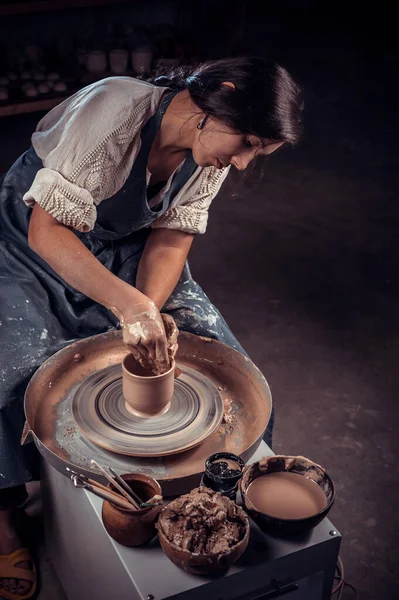 Yakından bakınca güzel bir çömlekçi kadın derin bir kase kahverengi kil yontuyor ve güzel bir atölyede çömlekçi çarkının üzerindeki fazlalıkları kesiyor. — Stok fotoğraf