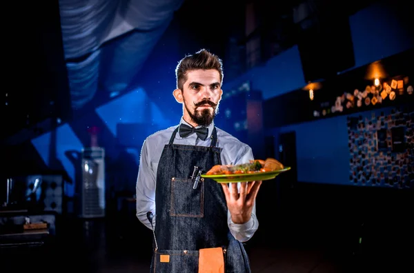 Whiskered σερβιτόρος προσφέρει στους επισκέπτες πιάτο σε μαύρο φόντο. — Φωτογραφία Αρχείου