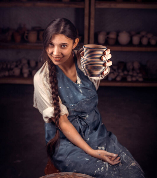 Ceramist girl shows the finished clay product in art studio. Handicraft industry.