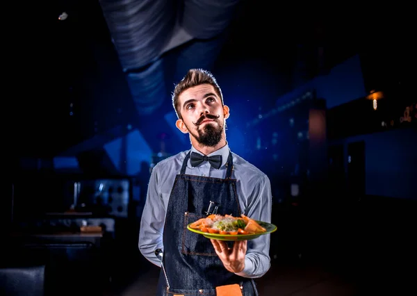 Νεαρός σερβιτόρος κρατά σαλάτα σε μαύρο φόντο. — Φωτογραφία Αρχείου