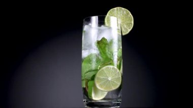 Limon dilimleri, nane yaprakları ve buz küpleriyle dönen bir mojito bardağı.