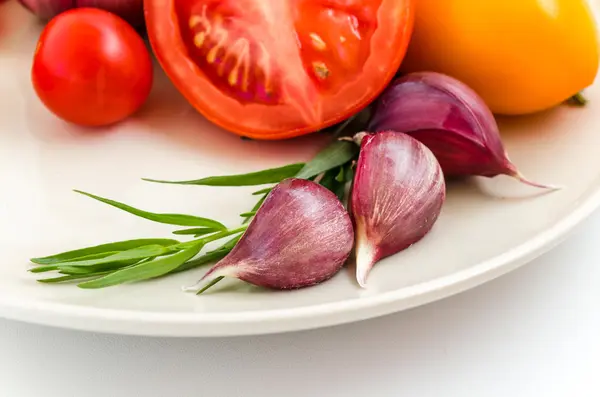 Fresh herbs, tomatoes and garlic on a white plate — Stock Photo, Image