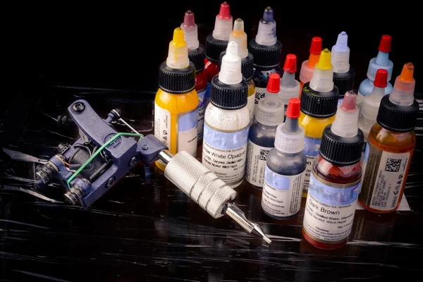 Tattoo machine with many color ink bottles isolated on black — Stock Photo, Image