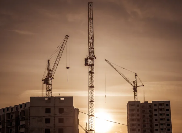 Guindastes de construção industrial e silhuetas de construção sobre o sol ao nascer do sol. — Fotografia de Stock