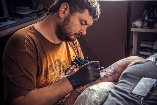 Homem usando luvas fazendo uma tatuagem no estúdio de tatuagem — Fotografia de Stock