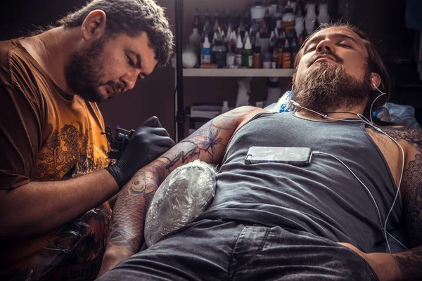 Tattoo master showing process of making a tattoo in tattoo parlour — Stock Photo, Image