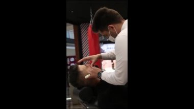 Bir berberin müşterinin sakalını keserken çekilmiş dikey videosu.