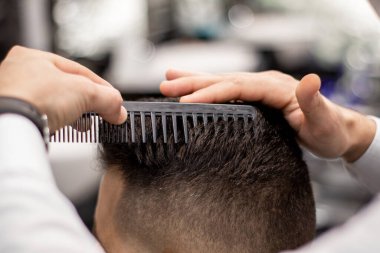 Berberin elleri beyaz bir adamın saçını tarıyor.