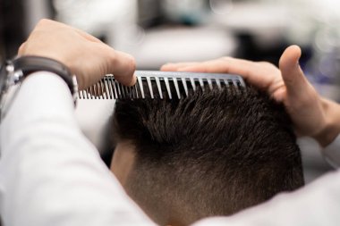 Berberin elleri beyaz bir adamın saçını tarıyor.