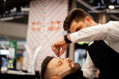 Papyonlu ve beyaz gömlekli berber müşteriyi tıraş ediyor.