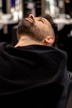 Müşteri boynunda siyah bir havluyla berber koltuğuna yaslanıyor.