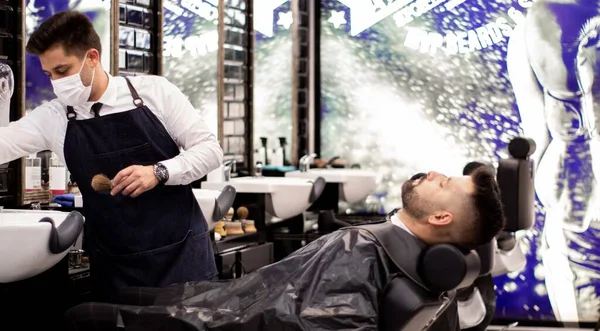 Client lying on a barber\'s chair while the barber pick up the brush