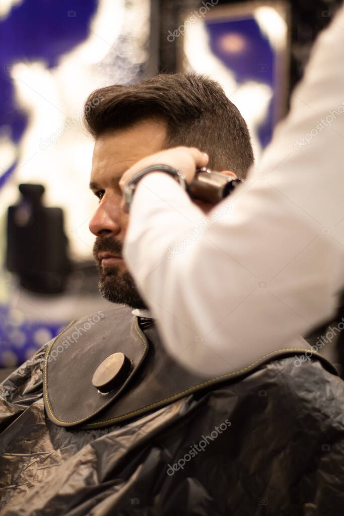peluquero joven y elegante con máscara corta el cabello de un cliente