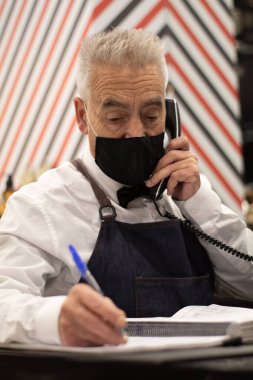 Berber dükkanının resepsiyonunda yaşlı berber telefonda konuşuyor.