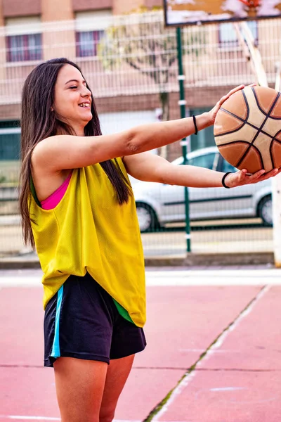 basketball player in a pink top sitting on an urban basketball court
