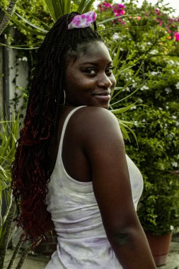 Beyaz elbiseli genç Afrikalı kadın kameraya bakarken gülümsüyor.