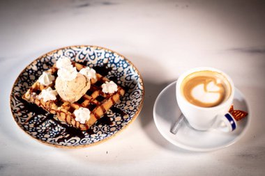 Waffle 'ın yanında dondurmayla süslenmiş karamelli lezzetli waffle çok güzel şekilli sütlü bir kahve..
