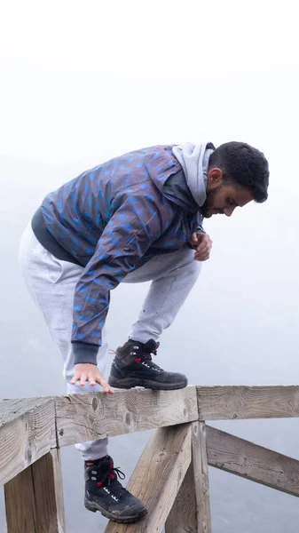 The young hiker jumps a wooden fence next to a fog-covered mountain.