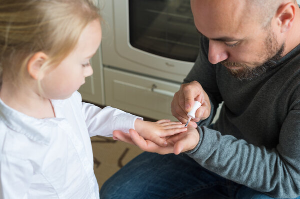 Father painting little daughters finger nails