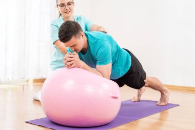 Physiotherapist working with young male client on core strength using fitball. Rehabilitation and physiotherapy background.	