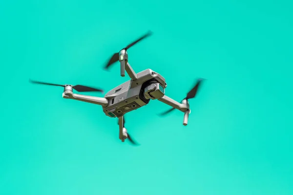 Flying drone with camera on turquoise background with copy space. Airborne quadcopter. Also known as a drone or UAV, Unmanned Aerial Vehicle. Low angle view.