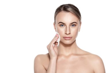 Makyaj malzemelerini çıkarmak için pamuk pedi kullanan güzel bir kadın gülümseyen kameraya bakıyor. Beyaz arka planda stüdyo çekimi. Güzellik ve cilt bakımı.