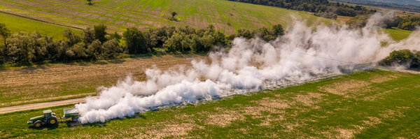 Aerial view of a tractor spreading lime on agricultural fields to improve soil quality after the autumn harvest. The use of lime powder to neutralize the acidity of the soil. Agricultural banner.