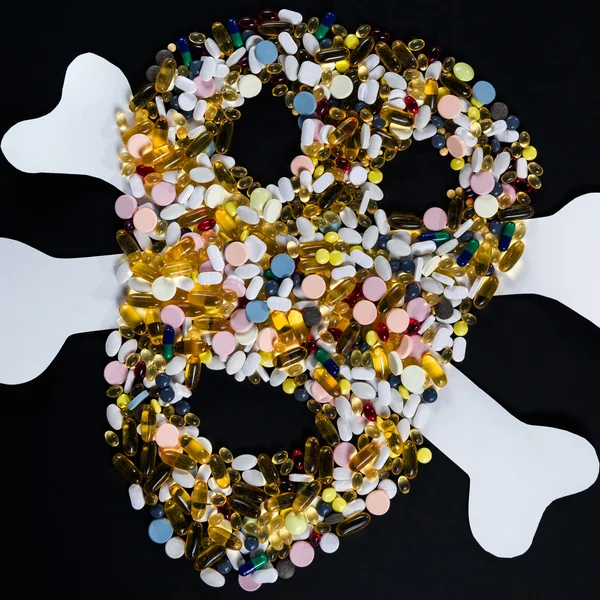 Tabletas, pastillas y cápsulas, que dan forma a un cráneo espeluznante, sobre fondo negro — Foto de Stock
