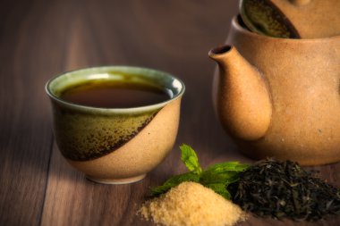 Seramik çaydanlık, siyah çay nane yaprakları ve ahşap masa üzerinde kahverengi şeker