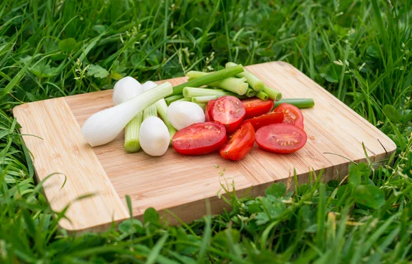 Färsk grön lök och körsbärstomater på den gamla trä skärbräda, närbild mat, skott utomhus — Stockfoto