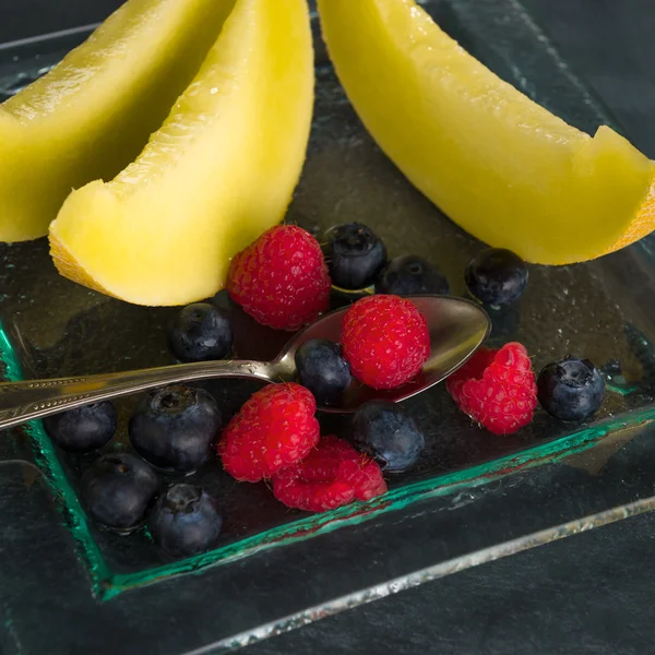 Fresh healthy fruit on a glass dessert plate on black background — Stock Photo, Image