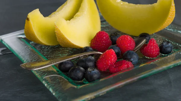 Fresh healthy fruit on a glass dessert plate on black background — Stock Photo, Image