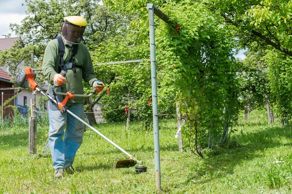 Samec zaměstnanec s moc nástroj řetězec trávníku strunovou sekačku sekání trávy — Stock fotografie