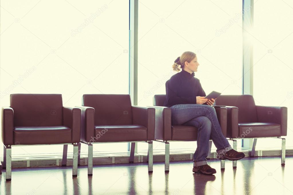 Young woman using her digital tablet pc at an airport lounge, modern waiting room, with backlight.