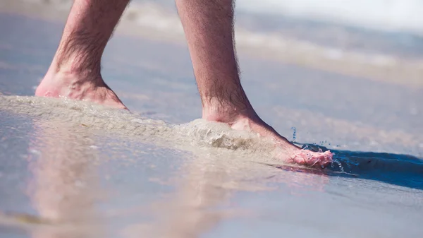 Manliga nakna fötter i en varm sand, man tar en promenad på en solig strand med turkost vatten under semester. — Stockfoto