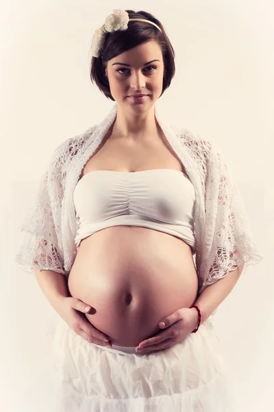 Aantrekkelijke jonge zwangere vrouw met naakte buik op witte achtergrond glimlachen — Stockfoto