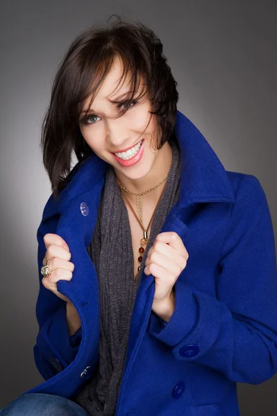 Vertikala färgbild av en vacker ung och självsäker kvinna skratta. Klädd i mörk blå vinterpäls. Studio porträtt. — Stockfoto