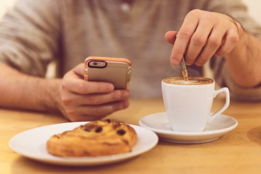 Her zaman temas halinde. Ayrıntılı görüntü kahve içme ve restoranda kahvaltı yaparken akıllı telefon tutarak tanınmayan adam.