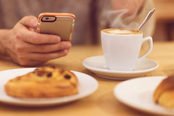 Sempre em contacto. Imagem de detalhe do homem irreconhecível bebendo café e segurando telefone inteligente enquanto toma café da manhã no restaurante . — Fotografia de Stock