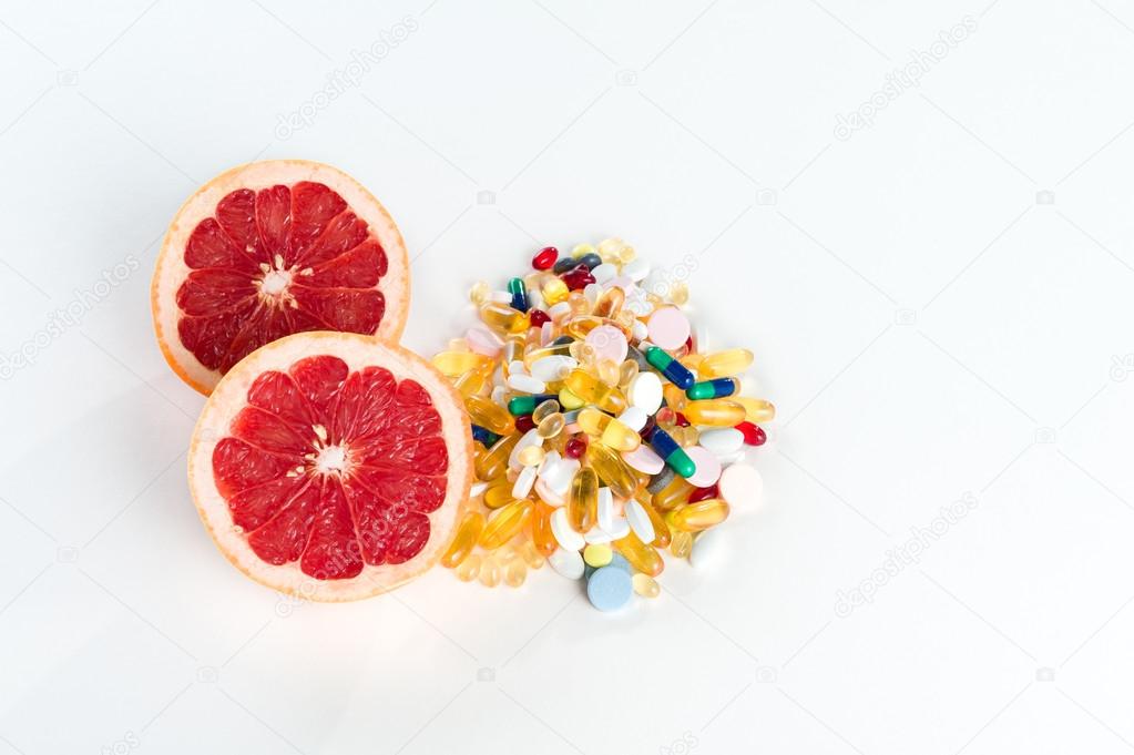 Pink grapefruit and pills, vitamin supplements on white background with copy space, healthy diet concept