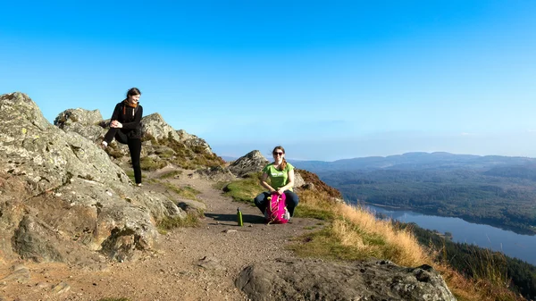 Duas caminhantes do sexo feminino no topo da montanha fazendo uma pausa e desfrutando de uma vista do vale, Ben A 'an, Loch Katrine, Highlands, Escócia, Reino Unido — Fotografia de Stock